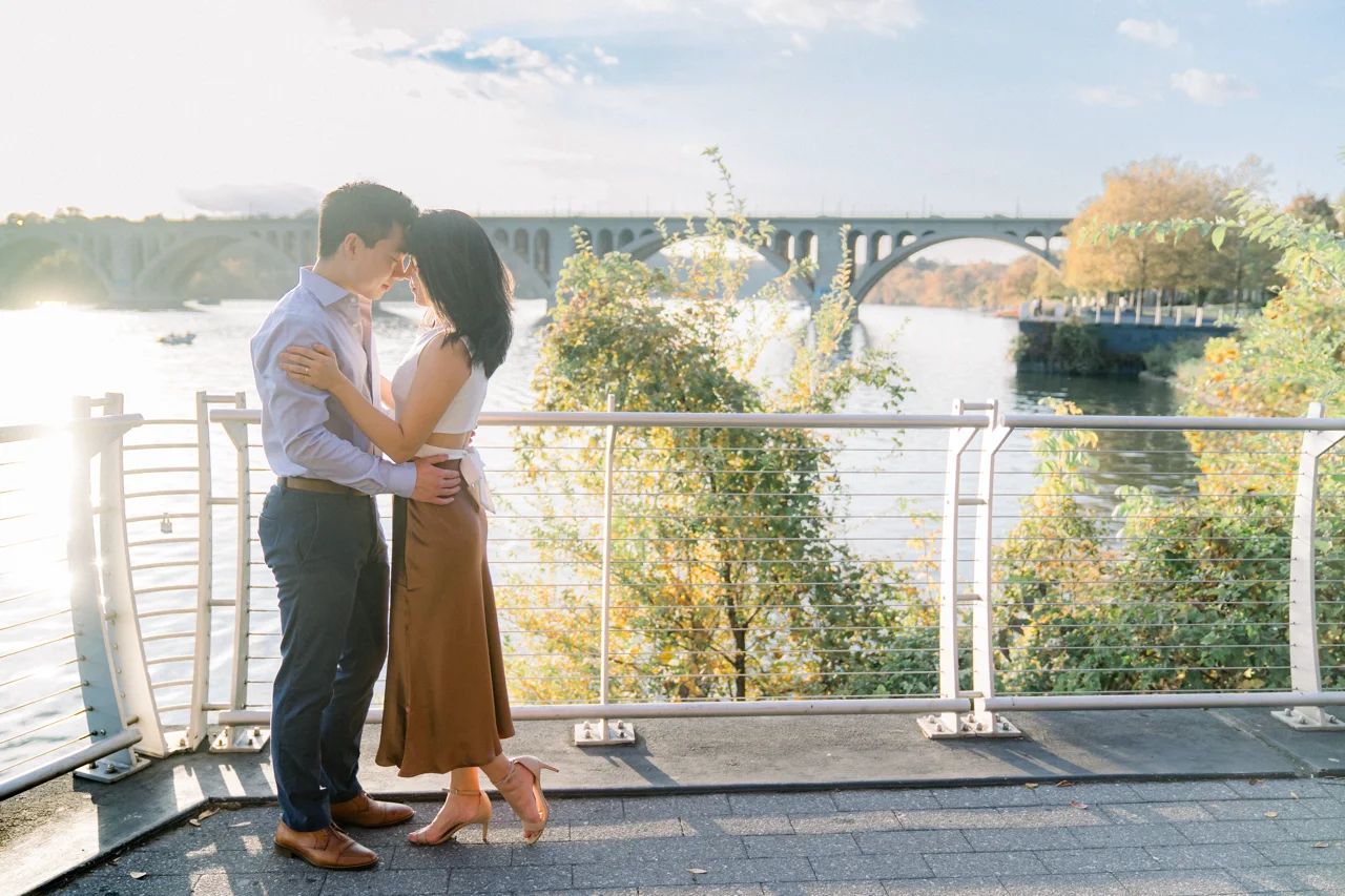 The couple embracing on the Georgetown promenade with the Potomac River in the background.